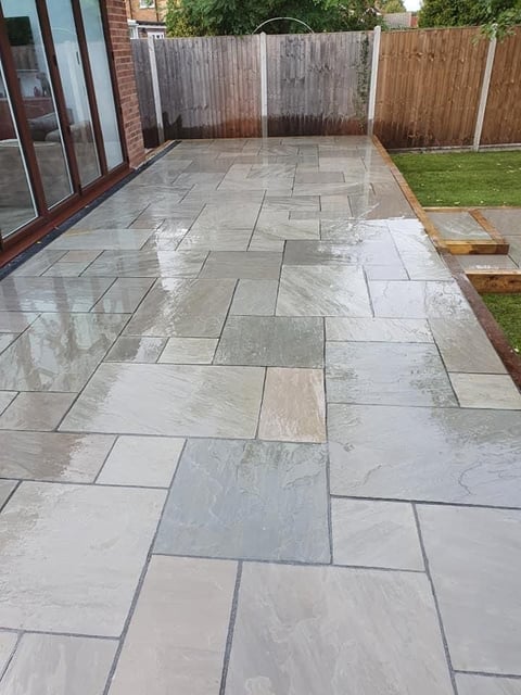 Wet slate patio with irregular stone pattern bordered by wooden fence and brick house exterior