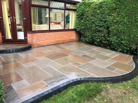 Curved patio with geometric stone tiles bordered by dark edging, adjacent to brick building and ivy-covered wall