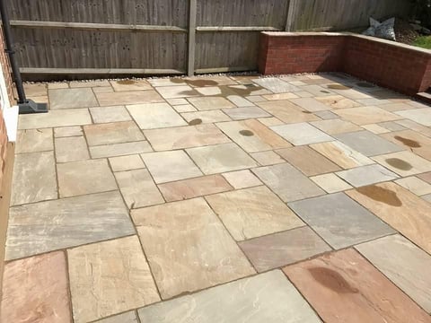 Empty patio with stone tiles in herringbone pattern, wooden fence in background