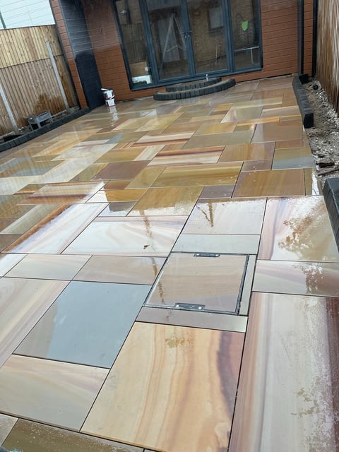 Patio with mixed natural stone and tile flooring in geometric patterns leading to a modern brick house with large windows