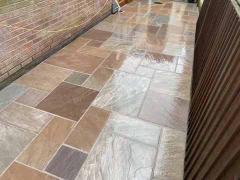 Wet outdoor patio with mixed stone and tile flooring in earth tones next to brick wall and metal gate