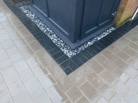 Dark blue garage door entrance with decorative white gravel border on black and gray tiled pavement