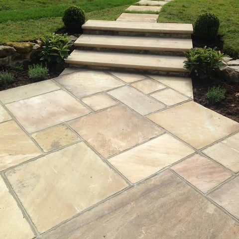 Paved garden pathway with stone steps leading upward through landscaped beds with topiary and lawn