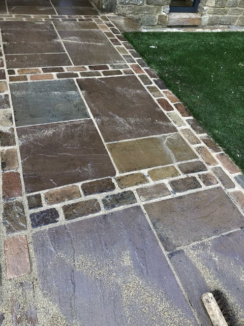 Outdoor patio with irregularly shaped stone pavers in various earth tones, adjoining a manicured green lawn