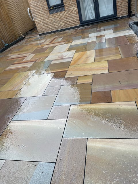 Wet patio with mixed-color rectangular pavers in herringbone pattern, brick building and windows in background